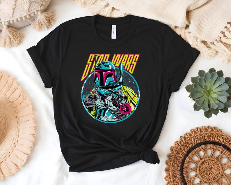 May include: Black t-shirt with a graphic of a Star Wars character in a circle. The character is wearing a helmet and holding a weapon. The words "STAR WARS" are printed above the character in yellow and orange.