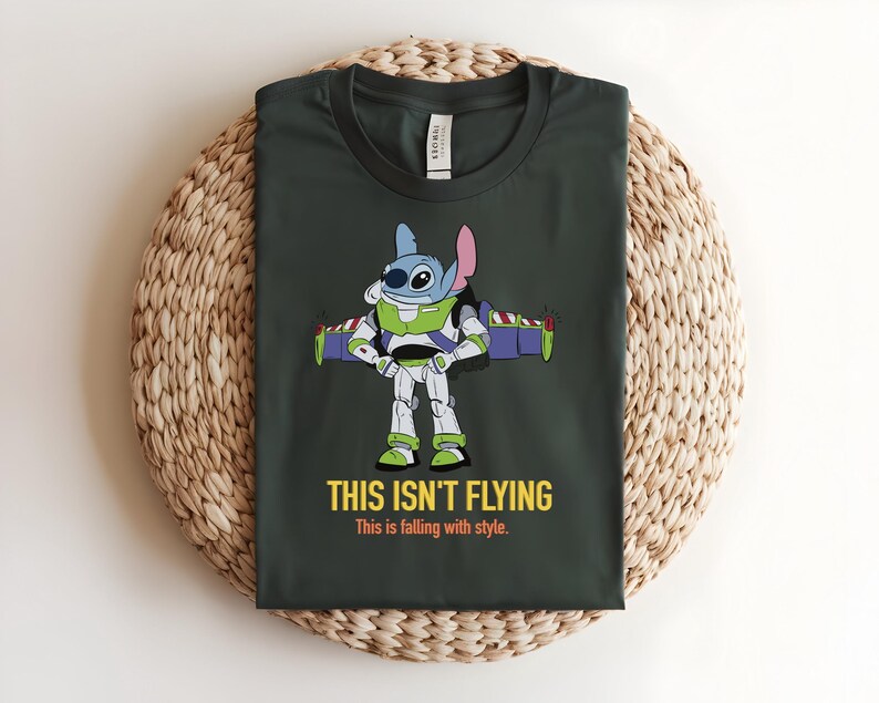 May include: Dark green t-shirt featuring a cartoon character fusion of Stitch and Buzz Lightyear. The character is wearing a Buzz Lightyear spacesuit with Stitch's features. The text "THIS ISN'T FLYING" and "This is falling with style" are printed below the character.
