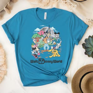 Puede incluir: Una camiseta turquesa con un gr&aacute;fico colorido de personajes de Disney, incluyendo Mickey y Minnie Mouse, Donald Duck y Goofy, frente al castillo de Cenicienta. El texto "Walt Disney World" est&aacute; impreso debajo.