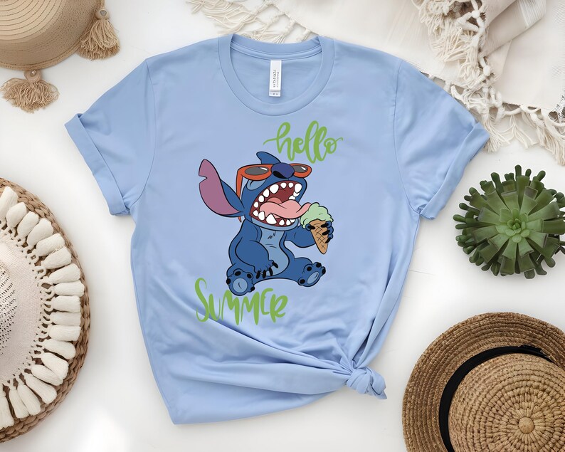 K&ouml;nnte beinhalten: Hellblaues T-Shirt mit einer Cartoonfigur, Stitch, die eine Sonnenbrille tr&auml;gt und Eis isst. Die Worte "hello summer" sind in gr&uuml;ner Schrift geschrieben. Das T-Shirt ist unten geknotet.
