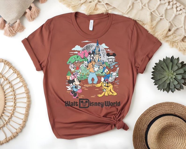 Puede incluir: Camiseta de color &oacute;xido con un gr&aacute;fico colorido de personajes de Disney, incluyendo Mickey Mouse, Minnie Mouse, Goofy, Donald Duck y Pluto, frente a un castillo. El texto "Walt Disney World" est&aacute; impreso debajo.