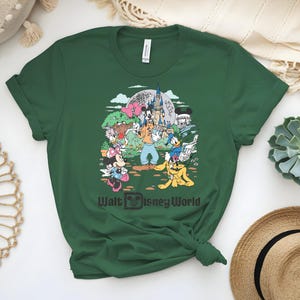 Puede incluir: Camiseta verde oscuro con un gr&aacute;fico colorido de personajes de Disney, incluyendo Mickey Mouse, Minnie Mouse, Donald Duck y Goofy, frente a un castillo. El texto "Walt Disney World" est&aacute; impreso debajo.