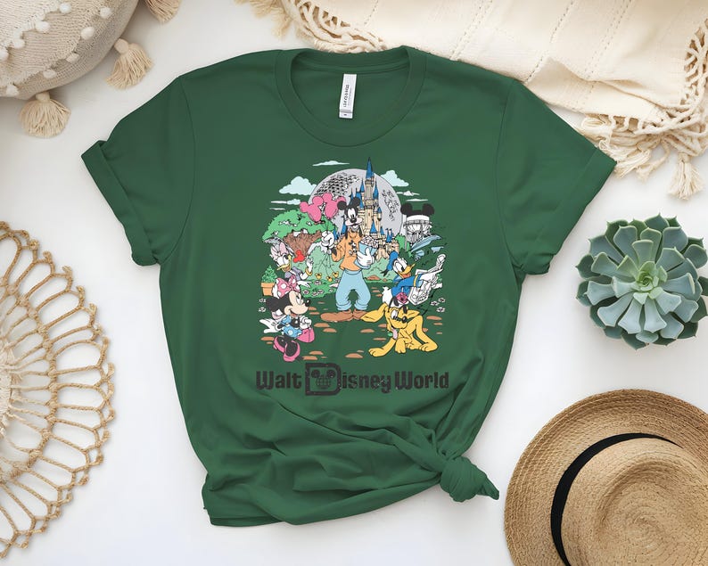 Puede incluir: Camiseta verde oscuro con un gr&aacute;fico colorido de personajes de Disney, incluyendo Mickey Mouse, Minnie Mouse, Donald Duck y Goofy, frente a un castillo. El texto "Walt Disney World" est&aacute; impreso debajo.
