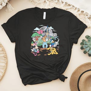 Puede incluir: Camiseta negra con un gr&aacute;fico colorido de personajes de Disney, incluyendo Mickey y Minnie Mouse, Goofy, Donald Duck y Pluto, frente a un castillo y una gran esfera. El texto "40 Years of Memories" est&aacute; en la parte inferior.