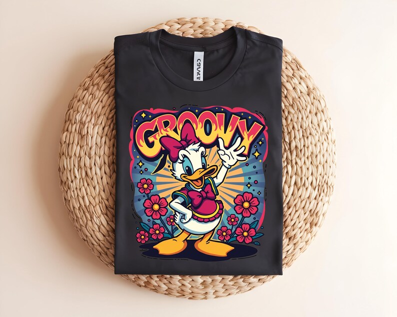 May include: Black t-shirt featuring a cartoon graphic of Daisy Duck with the word "GROOVY" in a colorful, retro font. Daisy is wearing a pink bow and vest, surrounded by flowers and a burst of rays.