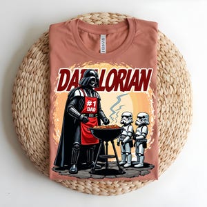 May include: A terracotta t-shirt with a graphic of Darth Vader at a barbecue. The design includes the text "DADORIAN" and "#1 DAD", plus Stormtroopers. The image is set against a sunset-like background.
