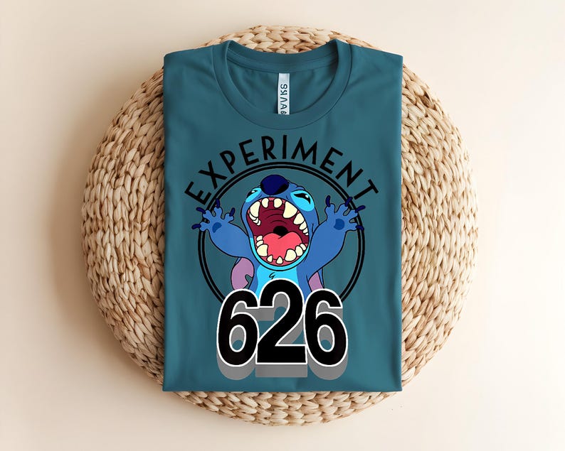 Pu&ograve; includere: T-shirt color teal con un personaggio dei cartoni animati e la scritta "EXPERIMENT 626". Il personaggio &egrave; blu con grandi orecchie e bocca aperta. Il testo &egrave; nero e il disegno &egrave; racchiuso in un cerchio nero.