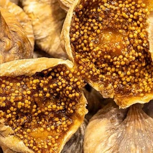 Peut inclure: Une collection de figues séchées à la peau extérieure ridée de couleur brun clair. Une figue est ouverte pour révéler une pulpe intérieure collante de couleur ambre foncé, densément remplie de nombreuses petites graines rondes jaune clair.