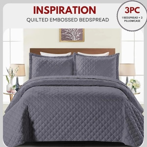 May include: A grey quilted embossed bedspread set with two pillowcases. The bedding set features a diamond pattern and is displayed on a bed with a wooden headboard. The text "INSPIRATION" and "3PC" are visible.