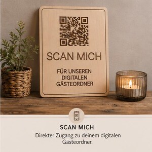 Könnte beinhalten: Rechteckiges Holzschild mit dem Text "SCAN MICH" und einem QR-Code. Darunter steht "FÜR UNSEREN DIGITALEN GÄSTEORDNER". Eine kleine Pflanze in einem geflochtenen Korb und eine brennende Kerze in einem Glas stehen auf einer Holzoberfläche.