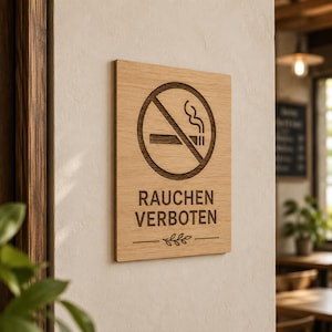 Può includere: Un cartello rettangolare in legno marrone chiaro con un simbolo di divieto di fumo inciso in marrone scuro e il testo RAUCHEN VERBOTEN in maiuscolo. Sotto il testo c'è un motivo a foglia inciso centrato tra due linee orizzontali.