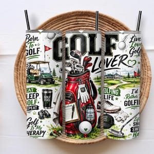 May include: A cylindrical tumbler with a straw featuring a golf-themed design. The print includes a red golf bag, a green golf cart, golf clubs, a ball, and text such as Born To Golf, Golf Lover, and Golf Is My Therapy on a white background.