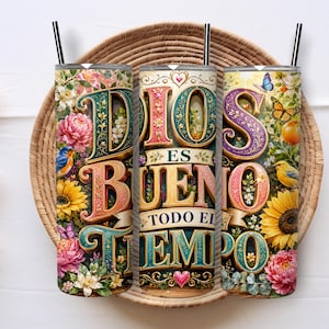 May include: Three cylindrical metal tumblers with black straws, featuring a colorful floral design with sunflowers, peonies, and birds. The text reads DIOS ES BUENO TODO EL TIEMPO in large, decorative, multi-colored 3D-style lettering with hearts.