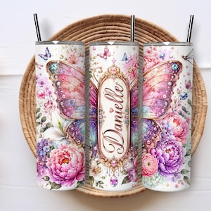 May include: Three cylindrical tumblers with black straws, featuring a vibrant butterfly and floral design in shades of pink, purple, and blue. The center tumbler displays the name Danielle in a decorative gold frame with jewel accents.
