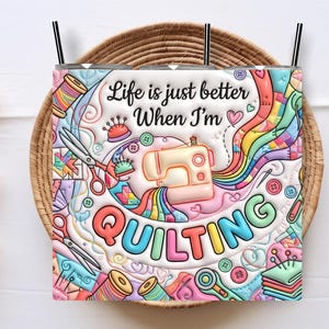 Pode incluir: Um copo colorido com tema de colcha. O design inclui uma máquina de costura, tesouras, carretéis de linha e o texto "Life is just better When I'm QUILTING". O copo tem uma palhinha e está sobre um fundo tecido.