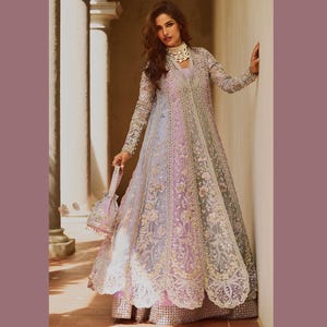 May include: A floor-length gown in pastel shades of lilac, pink, and grey, embellished with detailed embroidery and lace. The dress has long sleeves and a matching handbag. The style is elegant and suitable for formal occasions.