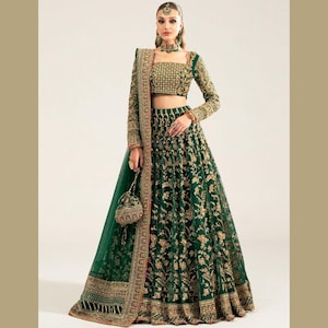 Pode incluir: Um lehenga verde escuro com bordados dourados. O traje inclui um top curto de manga comprida, uma saia longa e um dupatta a condizer. Uma pequena bolsa ornamentada é segurada. O lehenga é adornado com intrincados padrões dourados.