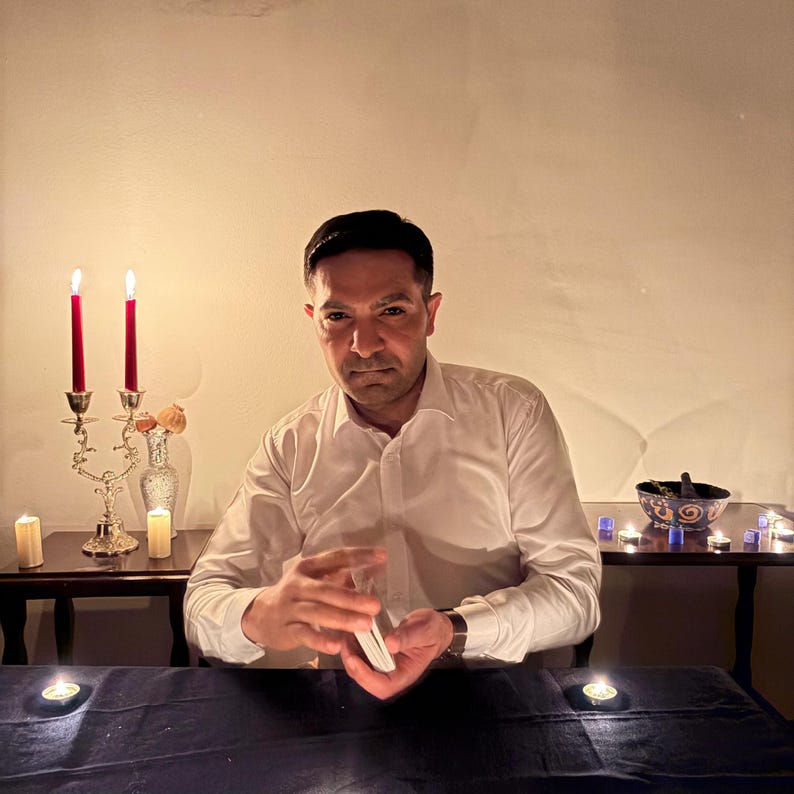 Puede incluir: Una persona con una camisa blanca sostiene una baraja de cartas. Dos velas rojas en un candelabro plateado y varias velas encendidas est&aacute;n sobre una mesa. Un peque&ntilde;o cuenco decorativo est&aacute; sobre una mesa en el fondo.