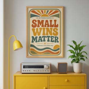 以下が含まれることがあります： 「TINY PROGRESS COLLECTION」、「SMALL WINS MATTER」、「Celebrate every little step.」という文字が書かれたレトロなデザインの額入りアートプリント。グラフィックには、日の出、波線、オレンジ、黄色、ティール色のカラーパレットが含まれています。