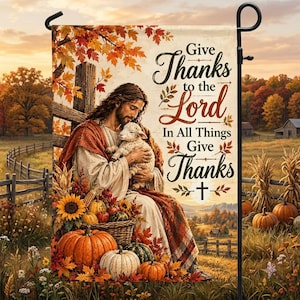May include: A rectangular garden flag featuring a figure with long hair and a robe holding a small white lamb. The text reads Give Thanks to the Lord In All Things Give Thanks. The scene includes autumn leaves, pumpkins, and a cross.