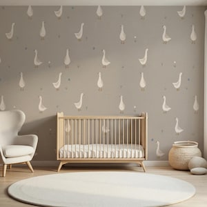May include: A nursery scene featuring a light wood crib, a white armchair, and a round, cream-colored rug. The wall is adorned with a repeating pattern of white geese on a neutral background. A woven basket and decorative stones complete the room.