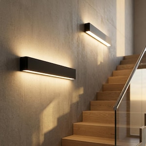 Puede incluir: Dos apliques de pared rectangulares negros con iluminación LED integrada están montados en una pared de hormigón. Los apliques están colocados encima de una escalera de madera con una barandilla de vidrio, creando una estética moderna y minimalista.