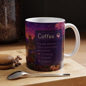 May include: A white ceramic coffee mug with a wrap-around design featuring a pixelated landscape and the word "Coffee." The mug includes text: "It smells delicious. This is sure to give you a boost." and stat boosts for energy, health, and speed.