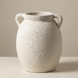 May include: A textured, off-white vase with two curved handles. The vase has a wide, rounded body and a slightly flared opening. The surface has a rough, stucco-like texture, giving it a rustic appearance. The vase is suitable for home decor.