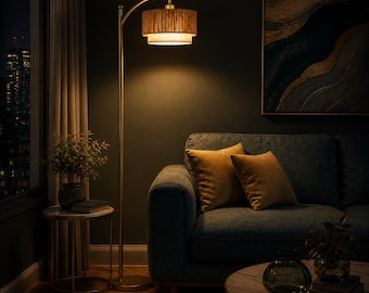 May include: A tall, slender floor lamp with a metallic gold finish and a curved arm. The lamp features a two-tiered, cylindrical drum shade made of textured, light brown natural fibers that emit a warm, soft glow downward into the room.