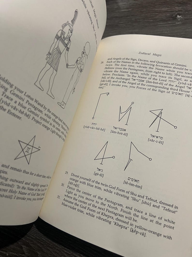 May include: Open book with illustrations and text about Zodiacal Magic. The pages show drawings of figures, symbols, and Hebrew text. Instructions are provided for rituals, including vibrating names and tracing sigils.