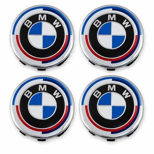 Puede incluir: Cuatro tapacubos plateados con el logotipo de BMW. Cada tapacubos presenta un círculo negro con las letras "B", "M" y "W" en blanco, que rodea un diseño de cuadrante azul y blanco. Una franja roja y azul rodea el logotipo.