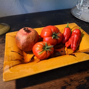 Könnte beinhalten: Ein rechteckiges, bernsteinfarbenes Keramiktablett mit dunkelbraunen, holzmaserungsartigen Streifen. Das Tablett enthält einen Granatapfel, zwei runde rote Tomaten mit grünen Stielen und drei längliche rote Chilischoten auf seiner Oberfläche.