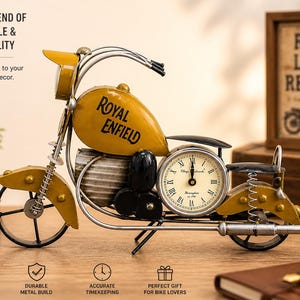 Könnte beinhalten: Eine dekorative gelb-silberne Metall-Motorraduhr mit dem Schriftzug "Royal Enfield" auf dem Tank. Die Uhr hat ein rundes Zifferblatt mit römischen Ziffern. Ein gerahmtes Schild hinter dem Motorrad lautet "Ride Live Repeat".