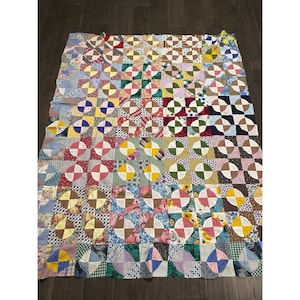 May include: A rectangular patchwork quilt featuring a repeating pattern of circular shapes formed by various fabric squares. The quilt displays a wide array of colours, including shades of blue, pink, yellow, green, brown, and white, with diverse floral, striped, and geometric prints.