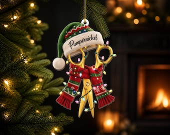 May include: A gold-colored pair of scissors ornament wearing a green and white knit hat with the text Pumpernickel and a red, green, and white patterned scarf. The scissors are wrapped in a string of small, multi-colored Christmas lights.