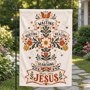 Könnte beinhalten: Eine cremefarbene Gartenflagge mit einem zentralen Blumenkreuz-Design in Orange-, Rot- und Dunkelgrüntönen. Der Text lautet: in the WAITING, in the HURTING, in the HEALING, in the SEARCHING, there was JESUS, verziert mit kleinen Bienen und Sternen.