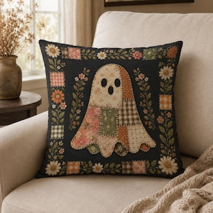 Peut inclure: Un coussin carré à fond noir présentant une figure de fantôme centrale composée de divers motifs de tissus en patchwork aux imprimés floraux, à carreaux et vichy atténués. Une bordure décorative de fleurs et de petits carrés encadre le fantôme.