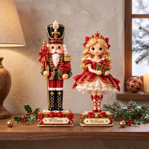 May include: A nutcracker figurine and a doll figurine, both standing on rectangular bases with the name William printed on the front. The nutcracker wears a black and red uniform, while the doll wears a red dress with white lace trim.