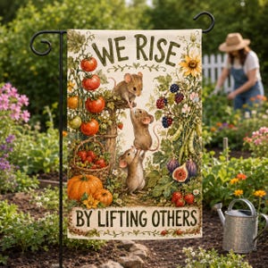 以下が含まれることがあります： WE RISE BY LIFTING OTHERSという文字が書かれた長方形のガーデンフラッグ。イラストには、木の柱のそばで互いに登り合う3匹の茶色のネズミが描かれており、トマト、イチゴ、ブラックベリー、イチジク、ヒマワリが周囲に配置されています。