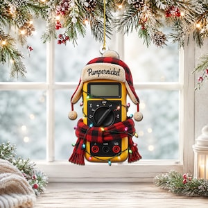 May include: A yellow digital multimeter hanging ornament wearing a red and black buffalo plaid trapper hat with a cream-colored brim and a matching red and black buffalo plaid scarf, wrapped in a string of colorful miniature Christmas lights.