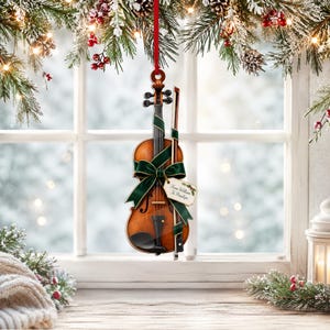 May include: A miniature violin Christmas ornament with a glossy brown finish, featuring a dark green velvet ribbon tied in a bow around the body. A small wooden bow is attached to the side, and a gift tag reads From William To Penelope.