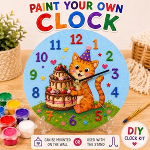 May include: A DIY clock kit featuring a cartoon cat with a birthday cake design. The clock face is light blue with colorful numbers and a cat wearing a party hat. The kit includes paint pots and a stand. Text on the clock reads "Paint Your Own Clock."