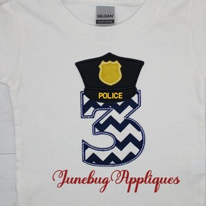 May include: White t-shirt with a blue and white chevron number three, a black police hat with a gold badge, and the text "Junebug Appliques".