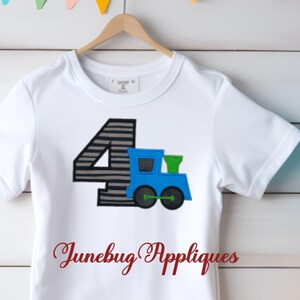 May include: White t-shirt with a gray and black number four and a blue train applique. The text "Junebug Appliques" is printed on the bottom of the shirt.
