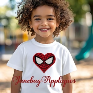 May include: A white t-shirt with a red heart-shaped applique featuring a Spiderman design. The text "Junebug Appliques" is printed in red below the applique.
