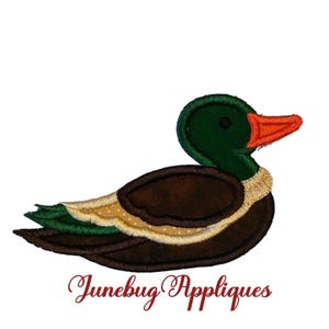May include: Green and brown embroidered applique of a duck with an orange beak. The applique is on a white background.