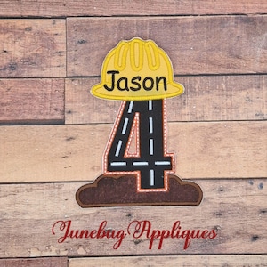 May include: A fabric applique featuring a yellow construction hard hat with the name Jason embroidered in black, positioned above a large black number four designed to look like a road with white dashed lines, resting on a brown dirt base.