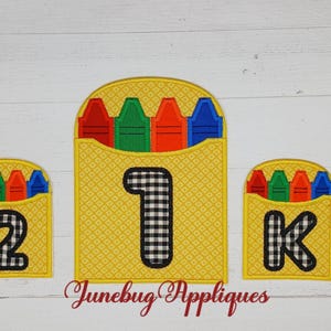 May include: Three yellow felt crayon holders with black and white checkered numbers 1, 2, and K. Each holder has five felt crayons in red, orange, yellow, green, and blue.