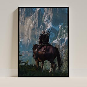 May include: A framed vertical wall art print depicting a white-haired figure in dark armor riding a brown horse. The rider carries two swords on their back, facing a massive, snow-capped mountain range with a stone fortress visible in the distance.