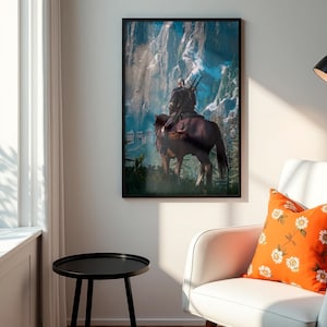 May include: A framed vertical wall art print featuring a digital illustration of a figure with long white hair riding a brown horse toward a snowy mountain range. The artwork is displayed in a black frame on a plain wall above a white armchair.